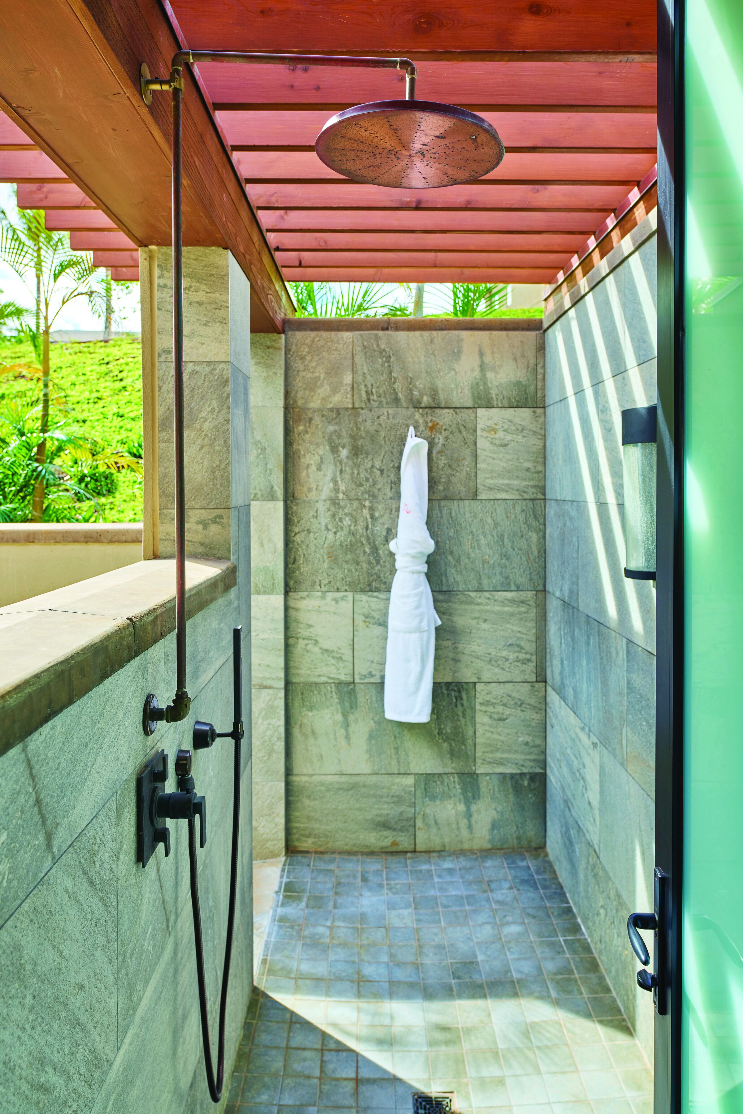 A shower area with a wooden ceiling, stone walls, and a towel hanging on the wall.