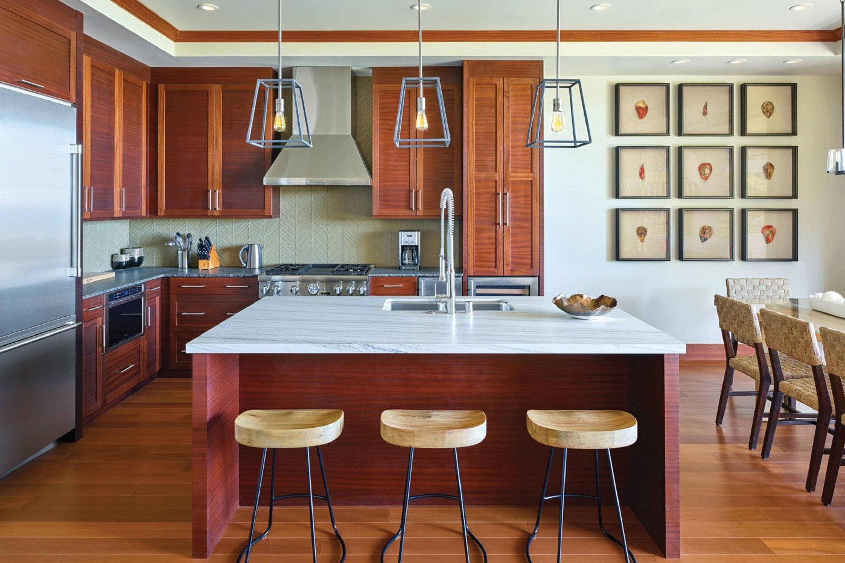 A modern kitchen with wooden cabinets, a large island with stools, stainless steel appliances, and pendant lighting.