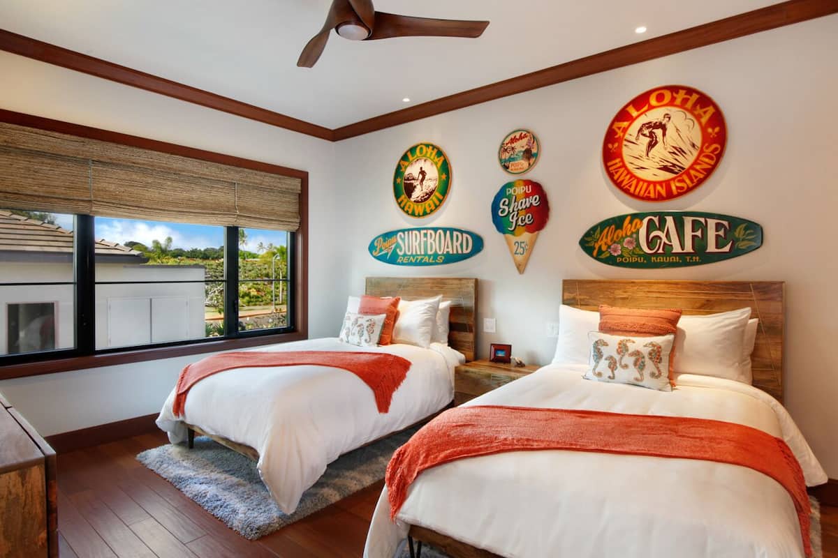 Une chambre d’hôtel avec deux lits, une grande fenêtre et des décorations murales comprenant des panneaux indiquant « Location de planches de surf » et « Aloha Café ».