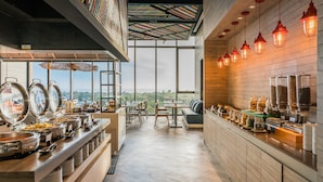 A buffet area with various food stations, a seating area with tables and chairs, and a view of the landscape through large windows.