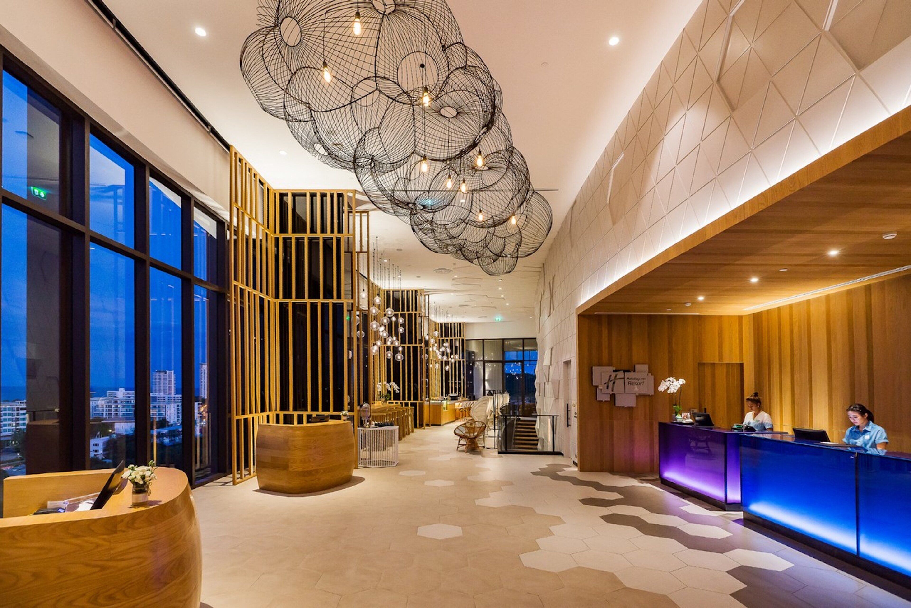 A hotel lobby with a reception desk, seating areas, and a large window offering a city view.