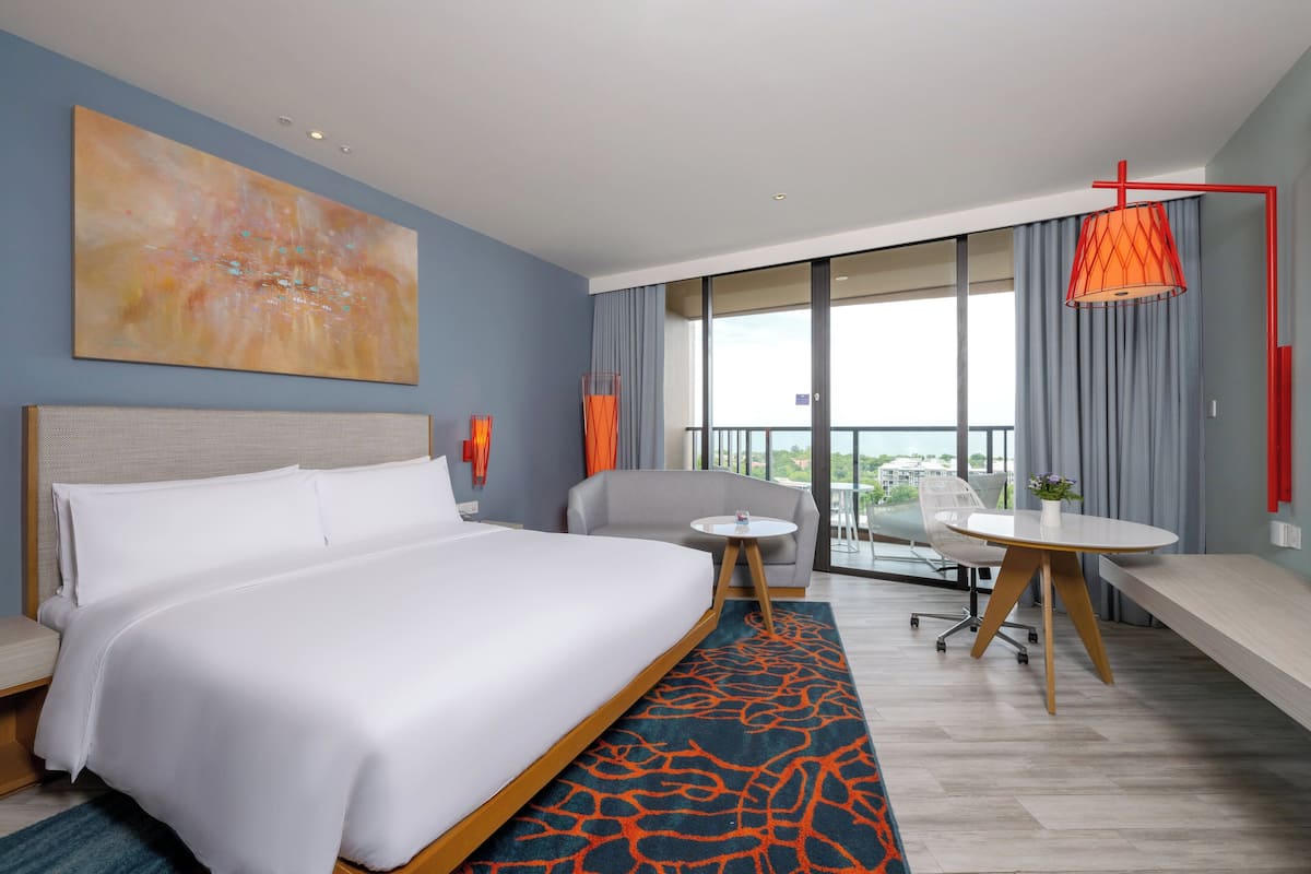 A hotel room with a large bed, a small round table, a sofa, and a balcony with a view.