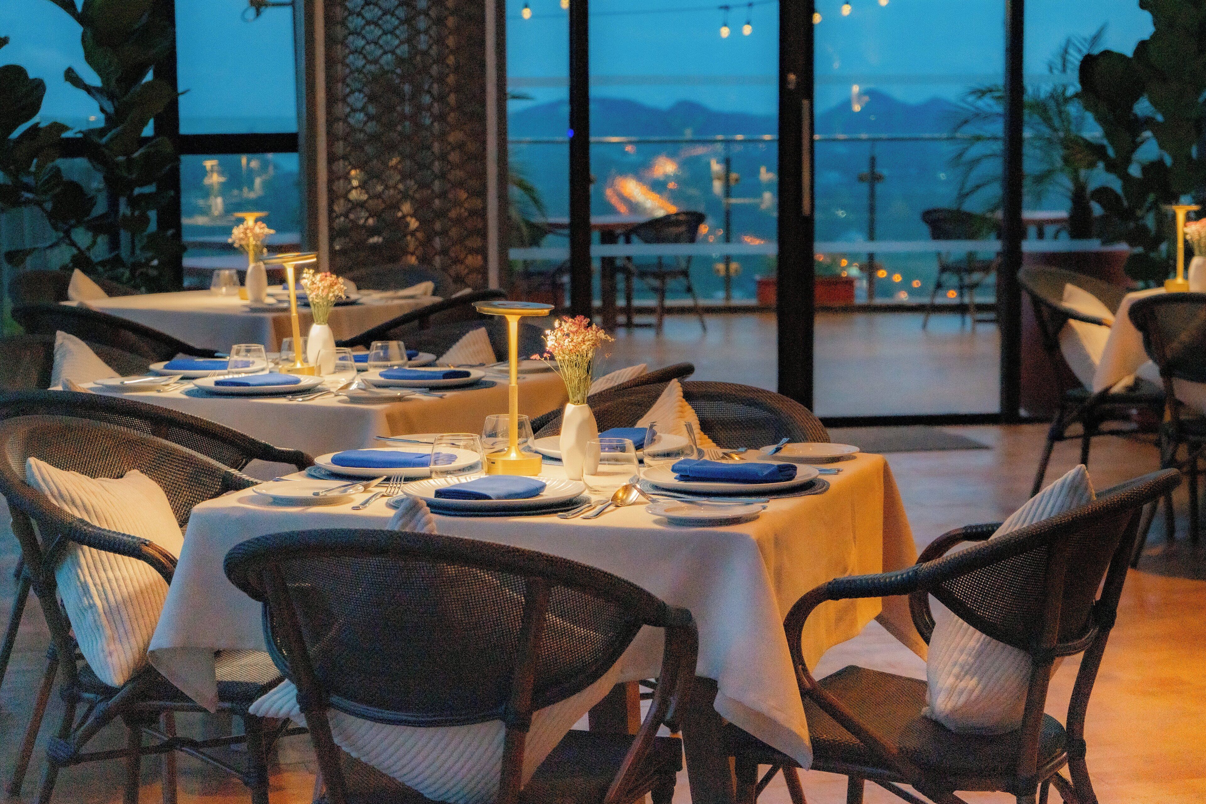 A restaurant with tables set for dining, featuring a view of the sea and mountains.