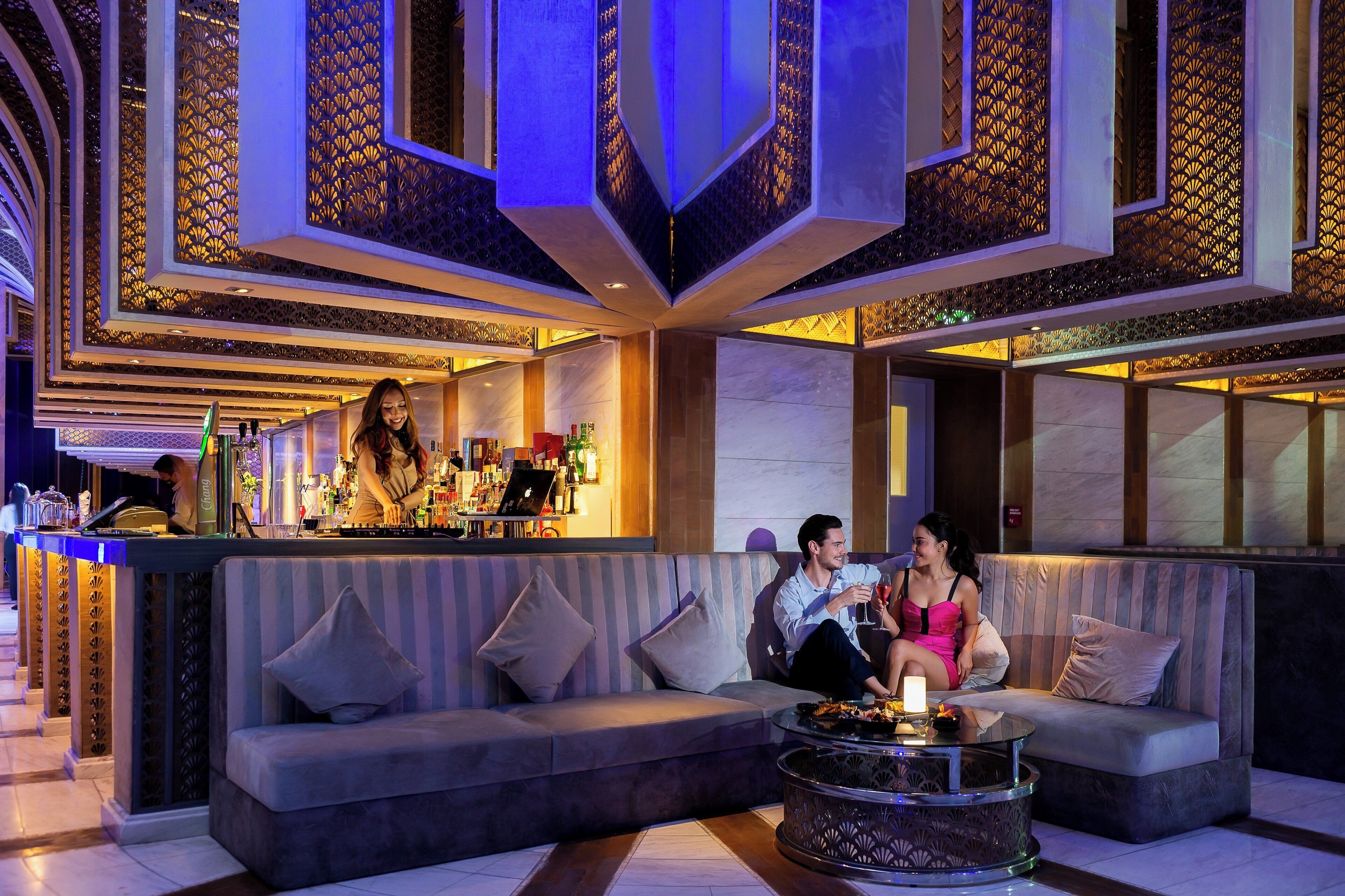 Un espace lounge moderne doté d’un bar, de sièges et de panneaux décoratifs au plafond.