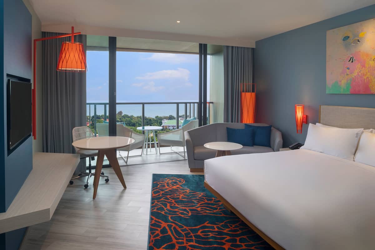 A modern hotel room with a large bed, a desk, and a balcony with a view.