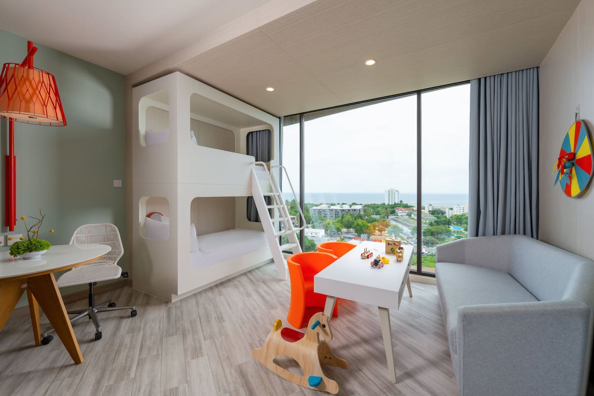 A modern child-friendly room with bunk beds, a play table, and a large window offering a city view.