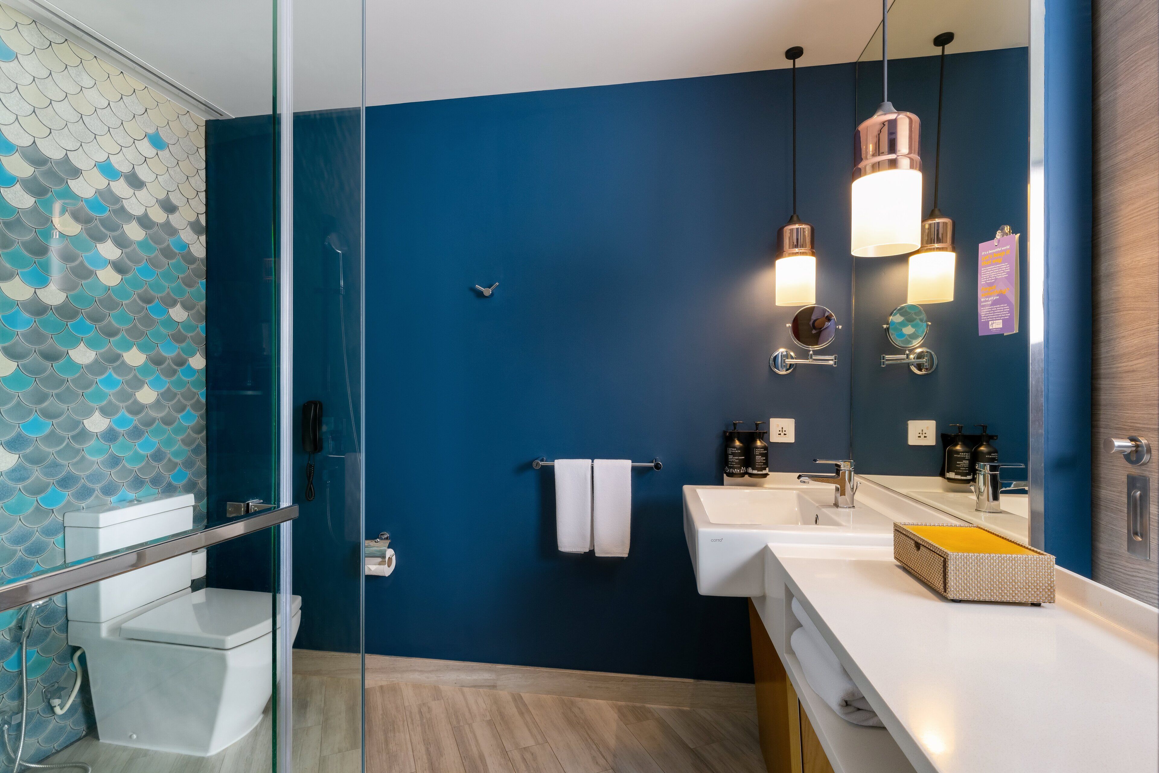 Ein modernes Badezimmer mit blauer Wand, zwei Waschbecken, einem großen Spiegel und einer Duschkabine aus Glas.