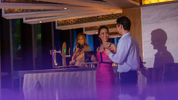 Una zona de bar con una barra, una persona vestida de rosa y otra con una camisa azul claro.