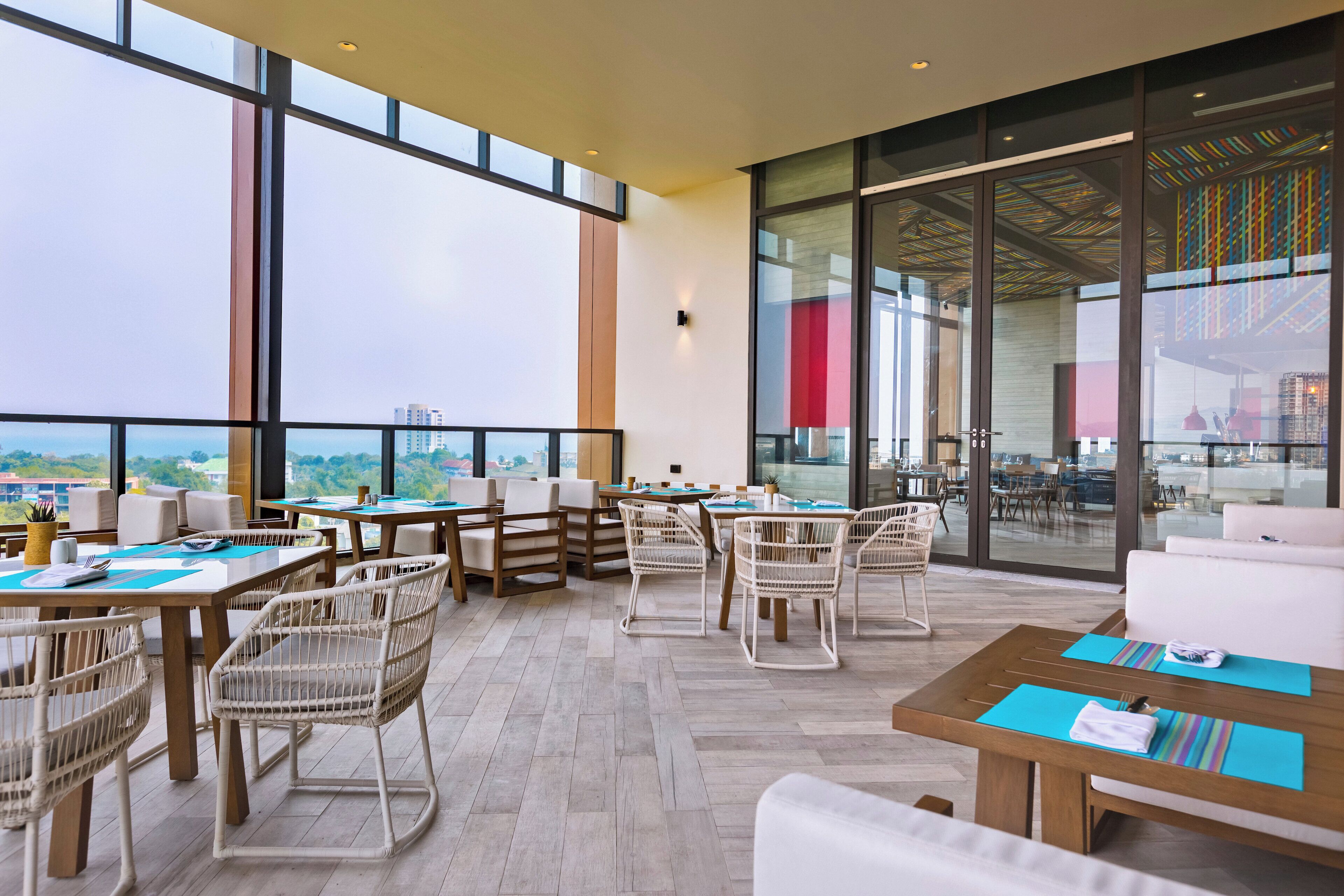 A spacious outdoor dining area with multiple tables and chairs, large windows offering views of the cityscape, and a modern architectural design.