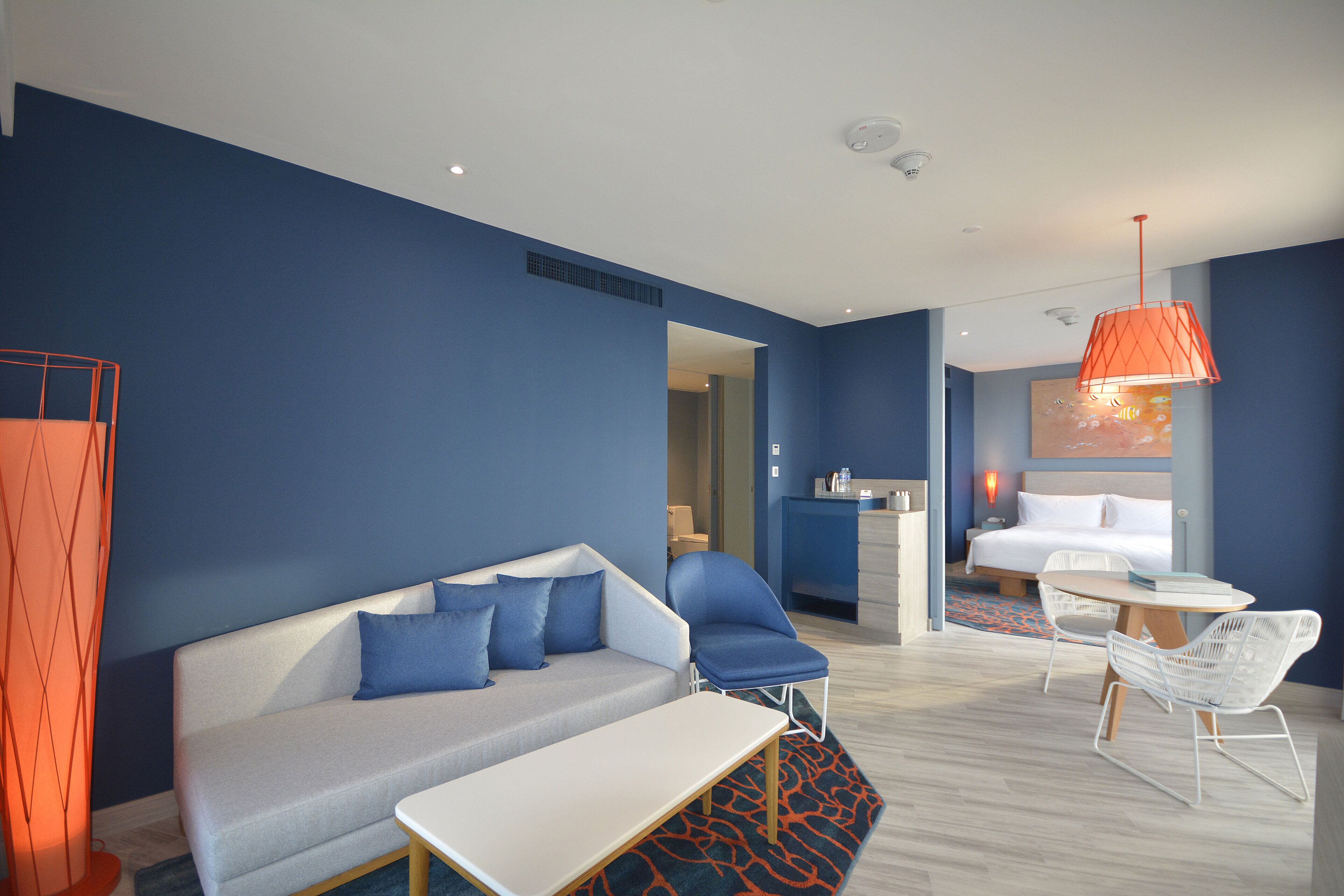 A modern hotel room with a sofa, chairs, a bed, and a dining area.
