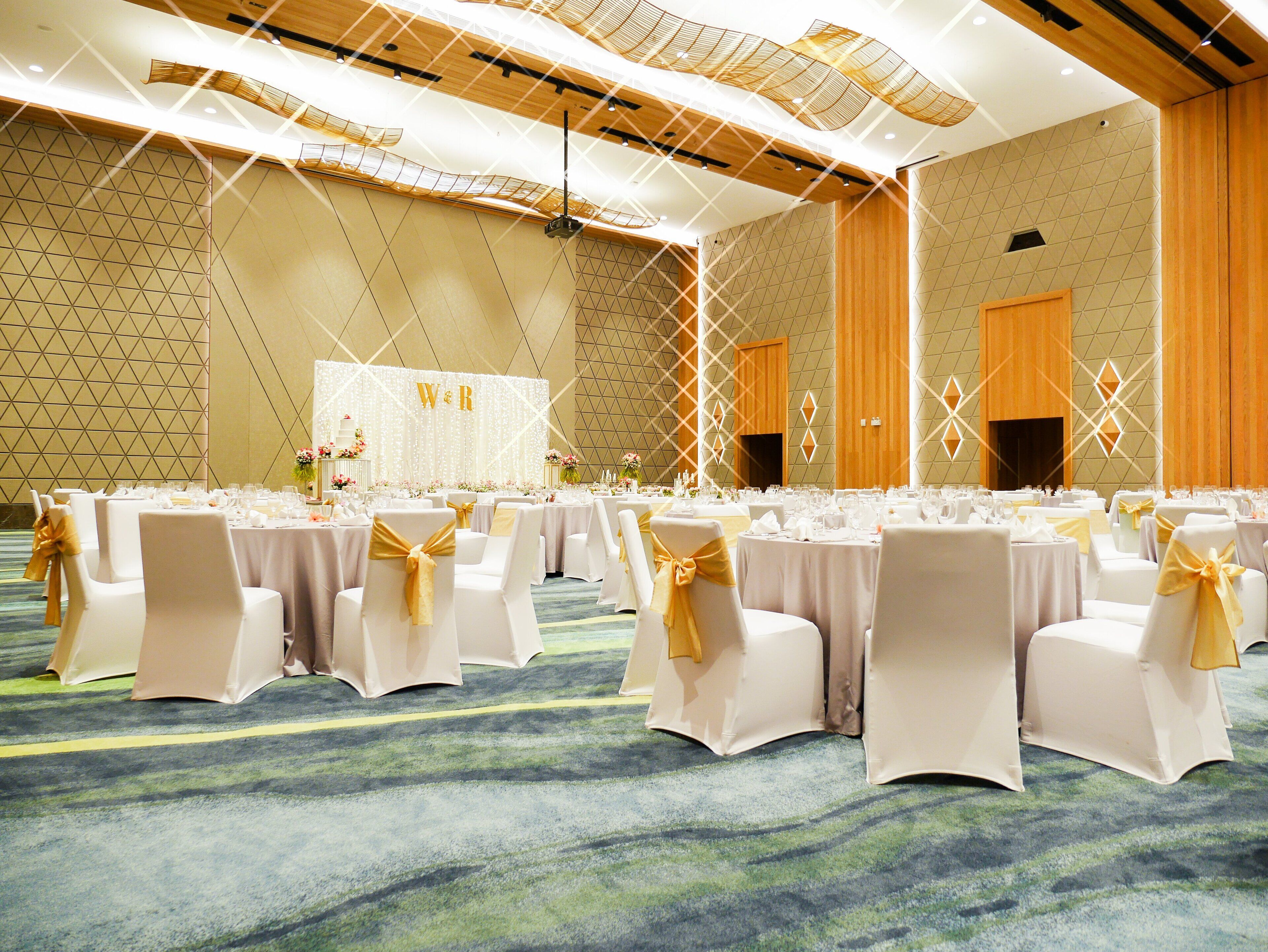 A banquet hall with round tables, white chairs with gold sashes, and a 'W & R' backdrop.