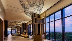 A spacious lobby with large windows, modern chandeliers, and a seating area.