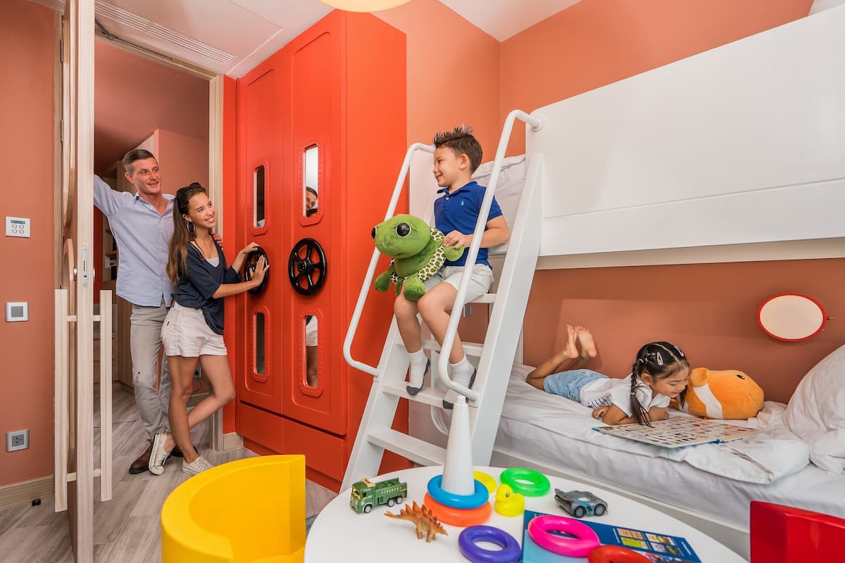 A child's bunk bed with a ladder, a play area with toys, and a red wardrobe.
