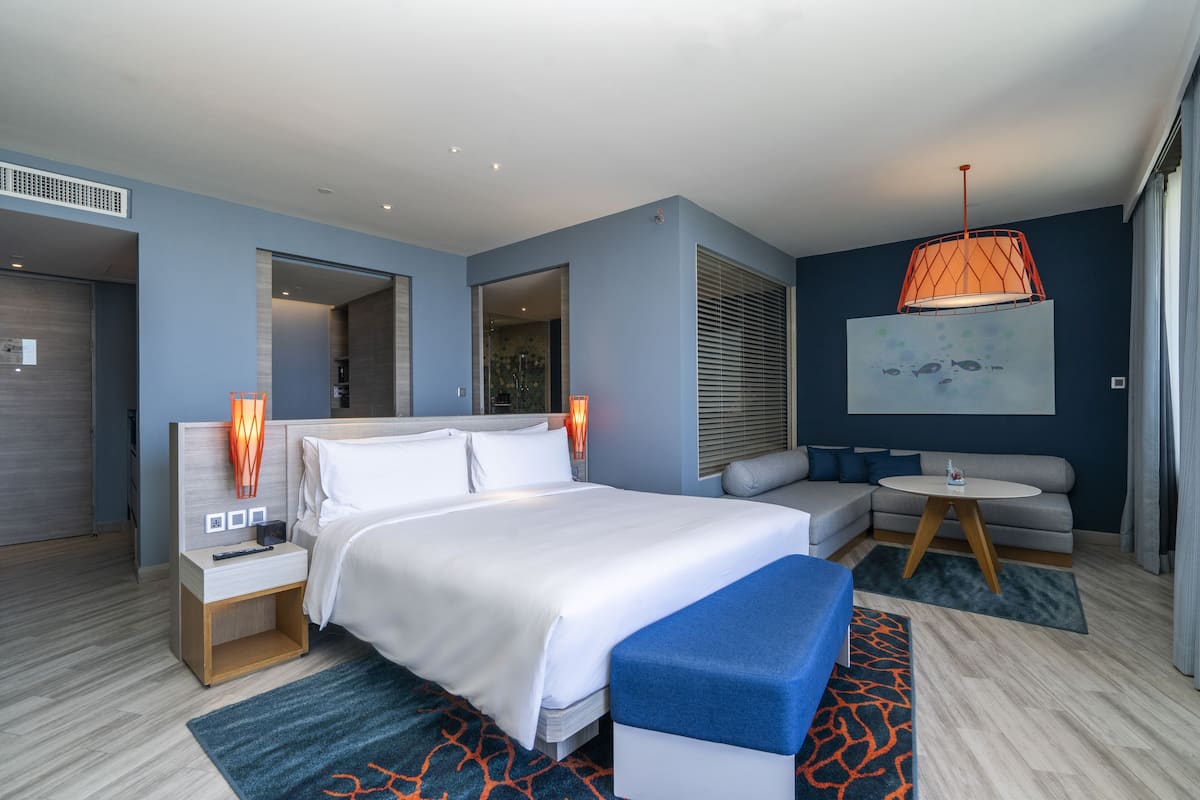 A modern hotel room with a large bed, a sofa, a small table, and a unique orange pendant light.