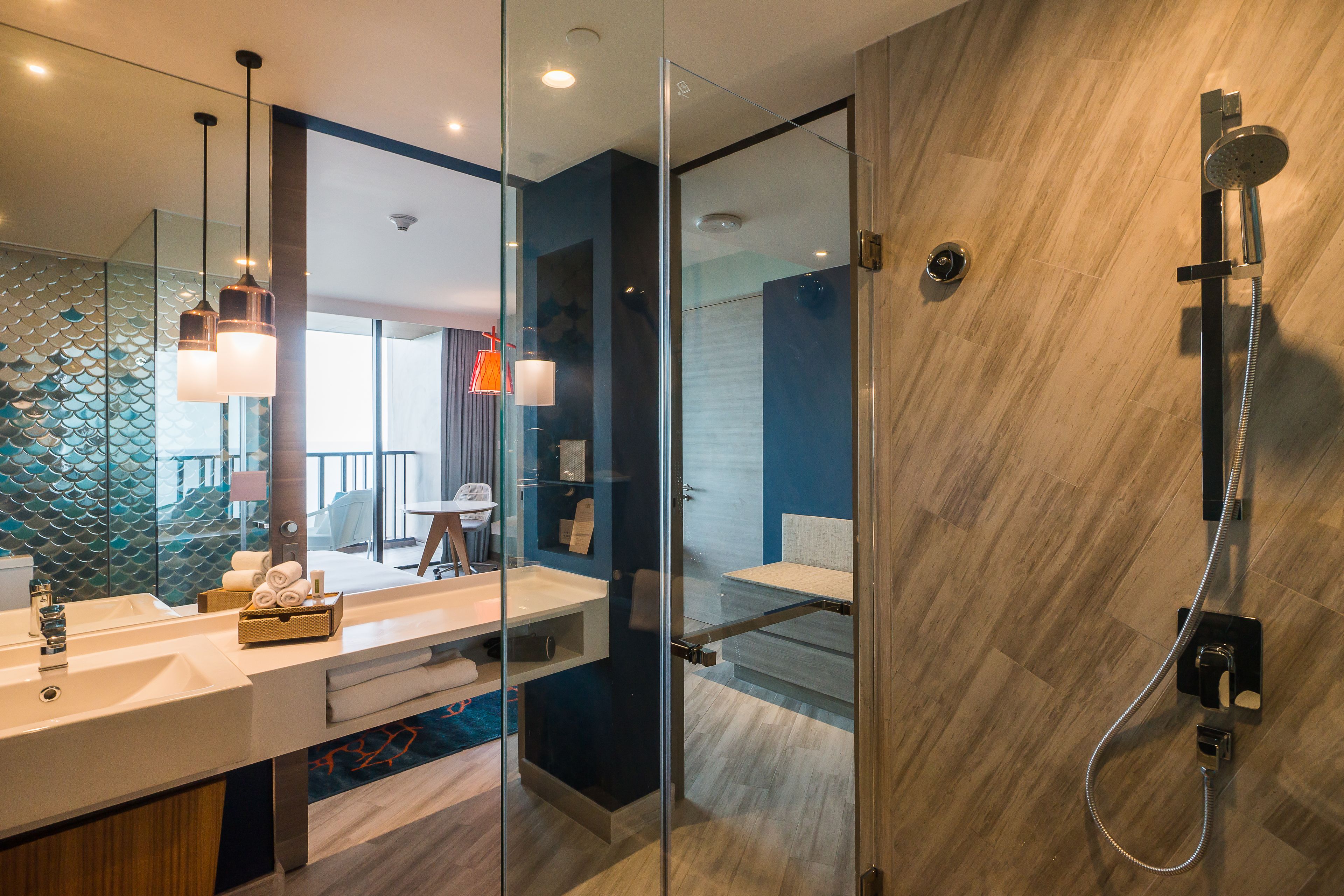 Une salle de bain moderne dotée d’une douche à parois de verre, d’un meuble-lavabo à deux vasques et d’un balcon visible à l’arrière-plan.