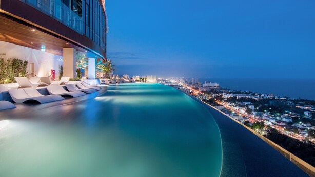 A rooftop infinity pool with lounge chairs, a city view, and a modern building facade.