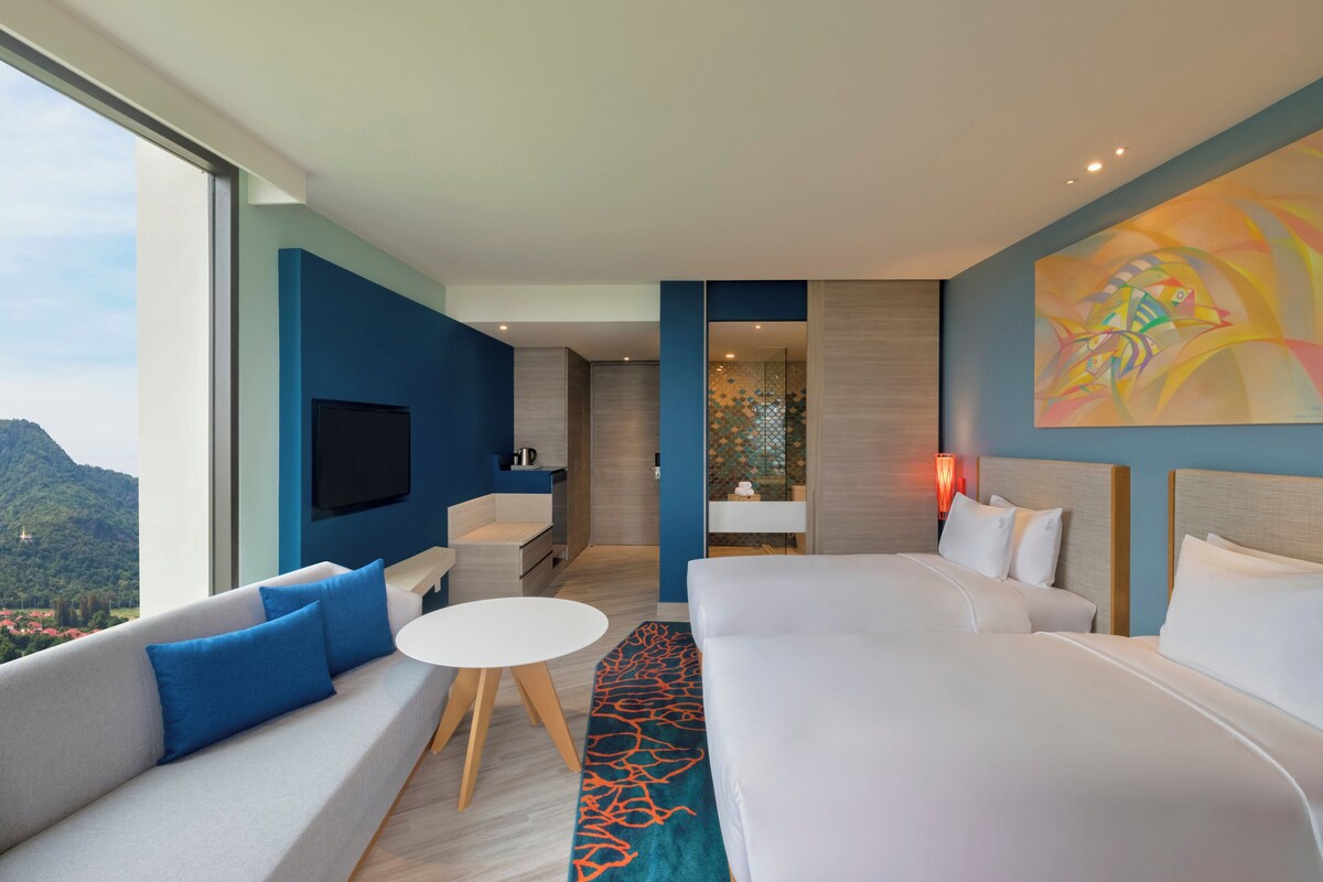 Quarto de hotel moderno com uma cama grande, um sofá, uma mesa pequena e uma televisão.
