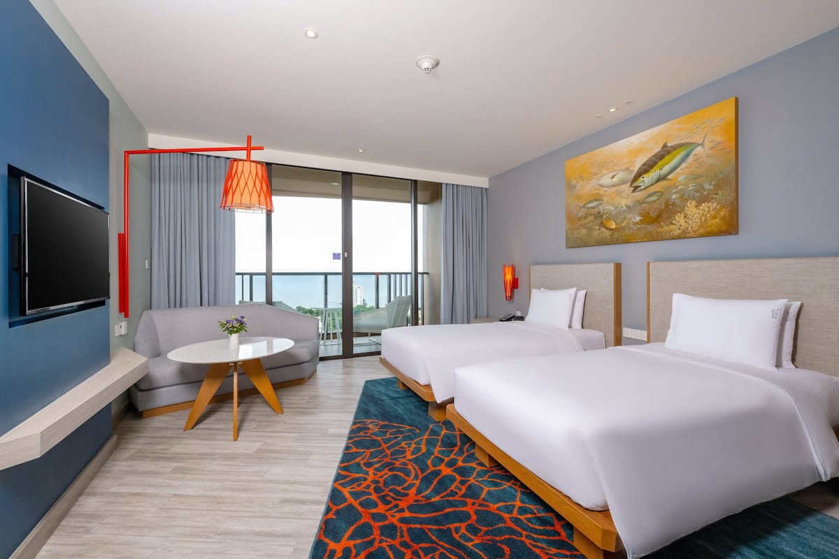 A hotel room with two beds, a TV, a balcony with a view, and a painting on the wall.