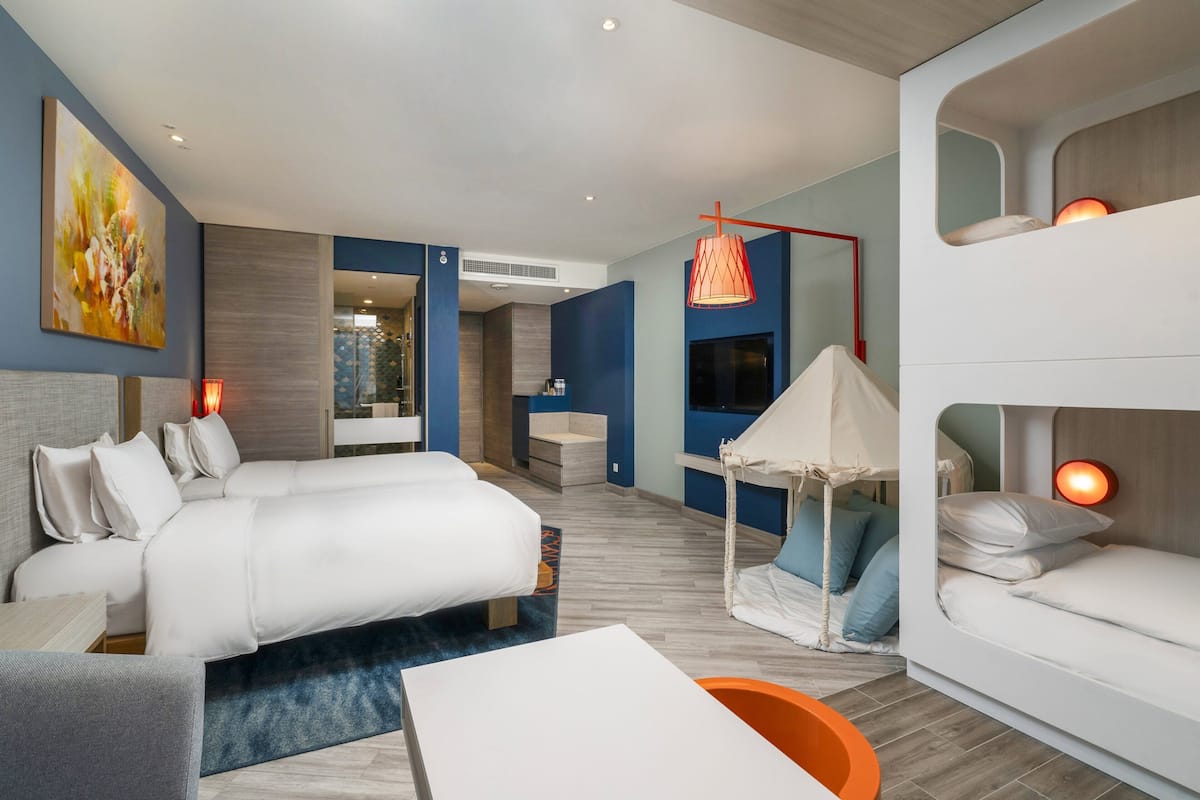 A modern hotel room with a large bed, a sofa, a desk, and a small seating area.