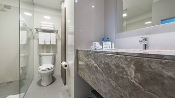 Een moderne badkamer met een douchecabine van glas, een toilet, een marmeren wastafel en een spiegel.