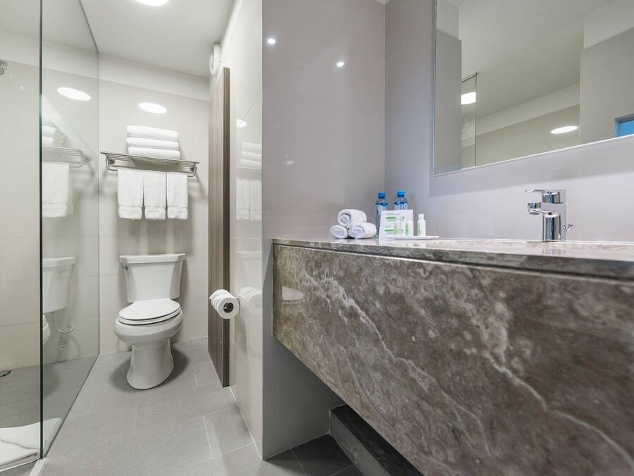 Een moderne badkamer met een douchecabine van glas, een toilet, een marmeren wastafel en een spiegel.