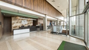 A modern hotel lobby with a reception desk, a staircase, and a large glass window.