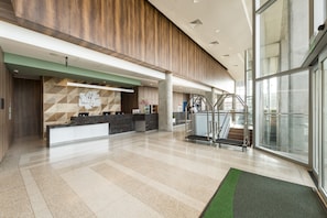 A modern hotel lobby with a reception desk, a staircase, and a large glass window. - Holiday Inn Lima Airport by IHG (Callao)