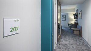 A hallway with a sign indicating room number 207, a teal-colored door, and a glimpse of a workspace area with a desk and chair. - Holiday Inn Lima Airport by IHG (Callao)