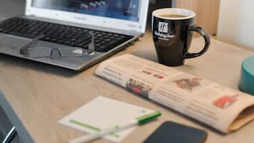 A laptop, a mug, a newspaper, and a pen on a wooden desk.