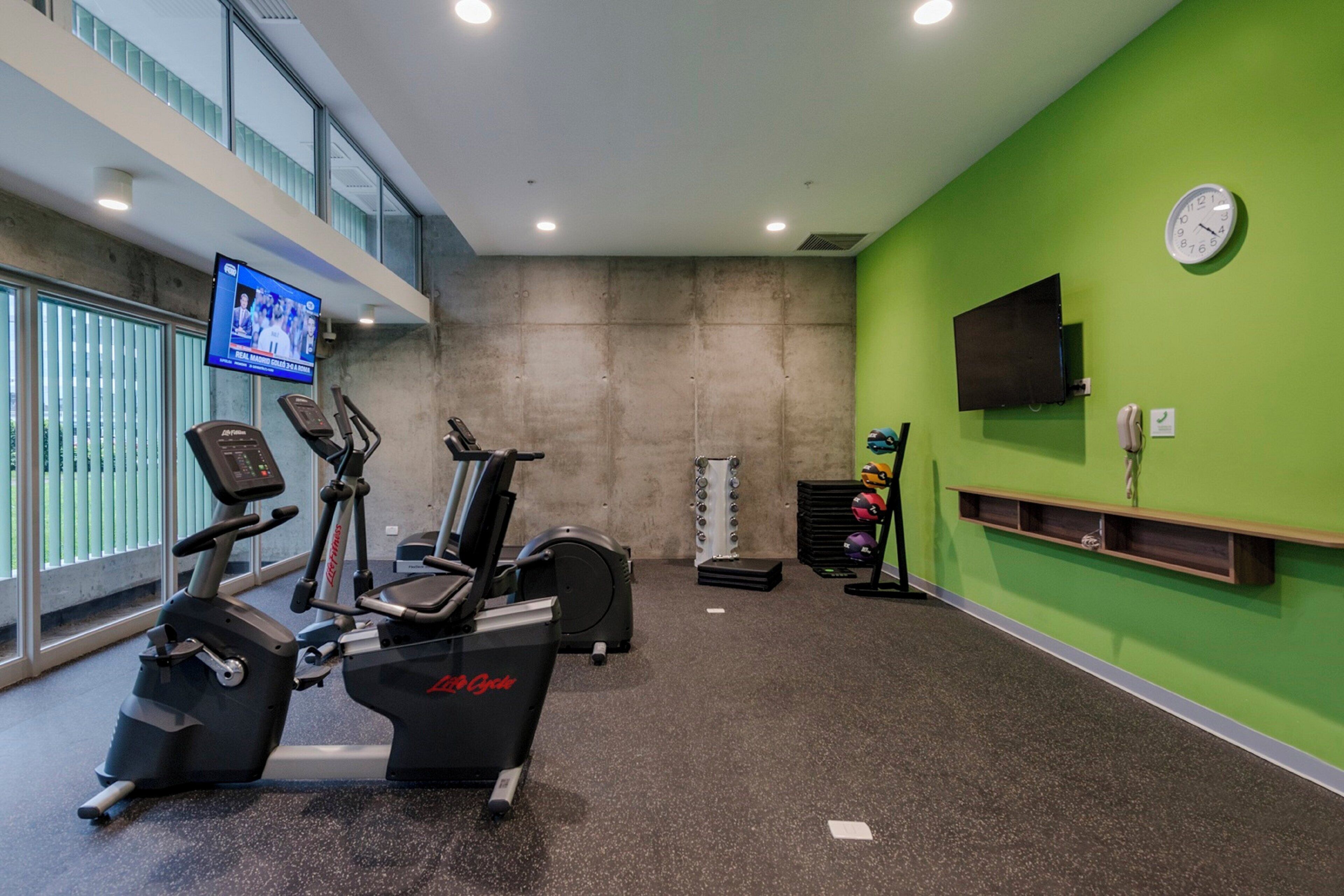 Une salle de sport équipée d’appareils de cardio-training, d’un téléviseur et d’une horloge murale.