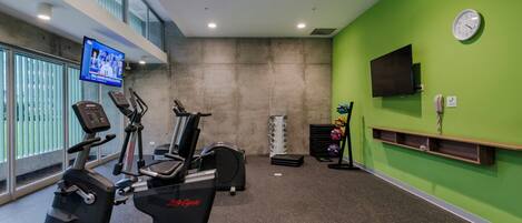 Une salle de sport équipée d’appareils de cardio-training, d’un téléviseur et d’une horloge murale.