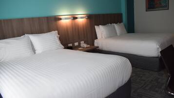 Hotellihuone, jossa on kaksi sänkyä, yöpöytä, jossa on puhelin, ja seinään kiinnitetty valaisin.