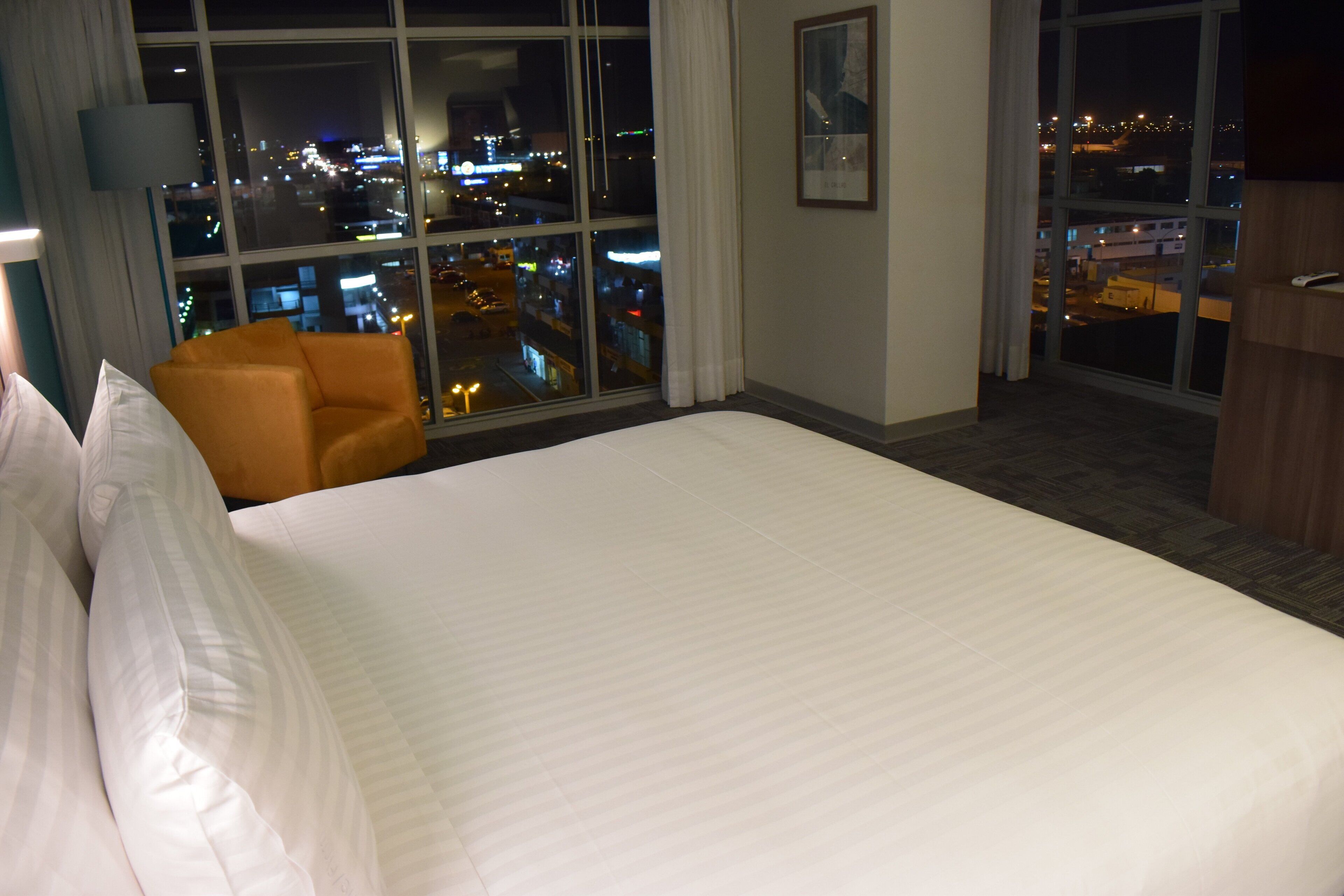 A hotel room with a large bed, a chair, and a view of a cityscape at night.