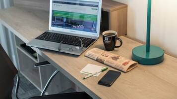Una computadora portátil sobre un escritorio con una taza de café, un teléfono inteligente, un bolígrafo y un periódico.