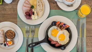 A breakfast setting with plates of eggs, sausages, and toast, a skillet with eggs, and a glass of orange juice.
