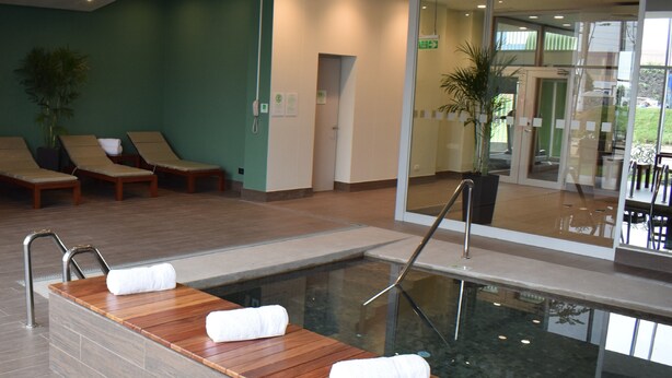 A modern indoor pool area with wooden loungers and a glass barrier. - Holiday Inn Lima Airport by IHG (Callao)