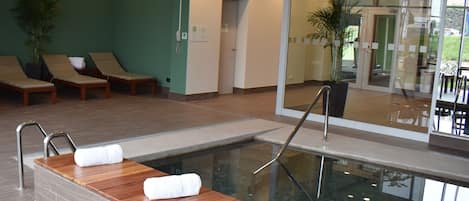Un área de piscina interior moderna con tumbonas de madera y una barrera de vidrio.