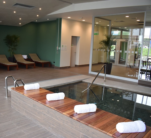A modern indoor pool area with wooden loungers and a glass barrier.