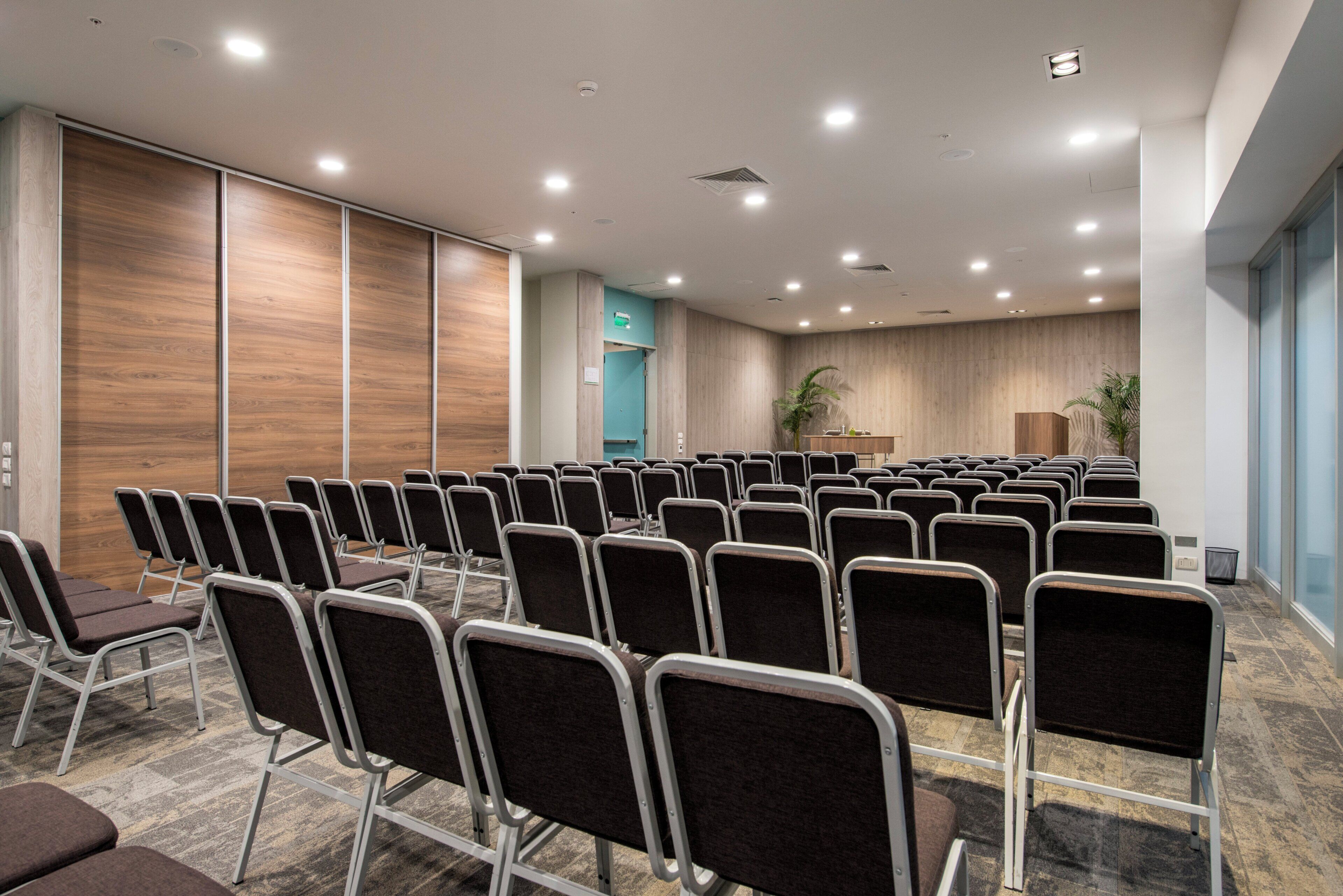 Un salón de conferencias con filas de sillas, un atril y una planta.