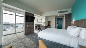 A hotel room with a large bed, a desk, a chair, a TV, and a view of the city. - Holiday Inn Lima Airport by IHG (Callao)