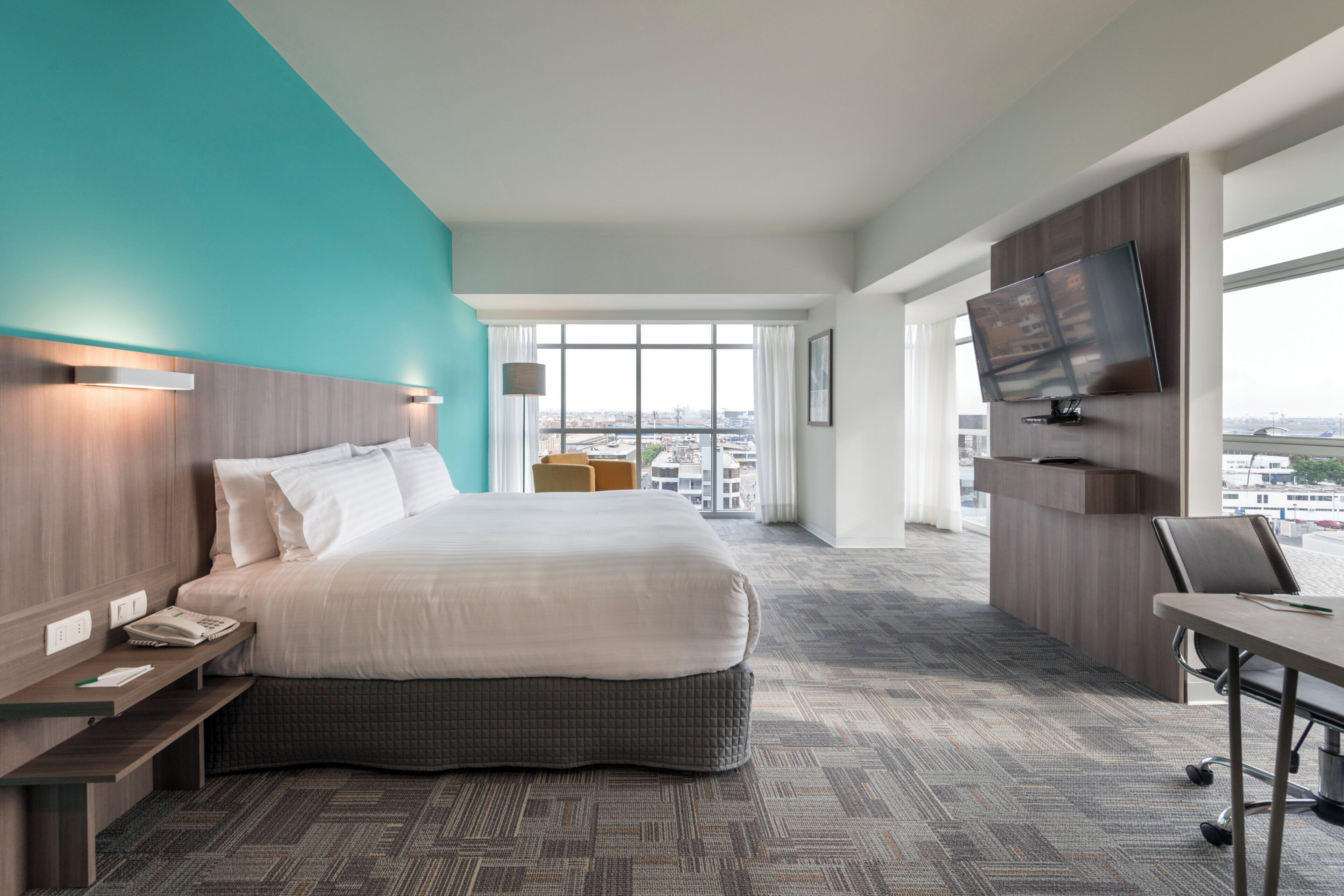 A hotel room with a large bed, a desk, a television, and a view of the city.