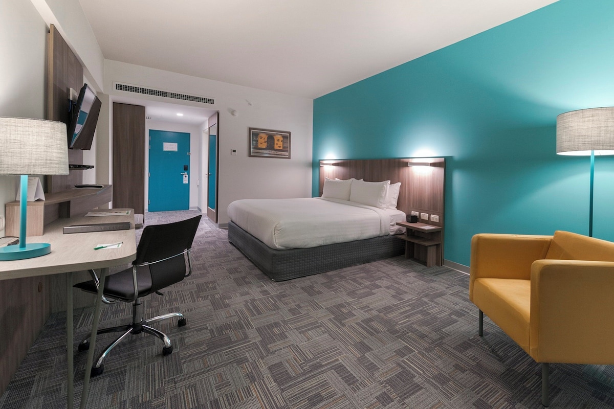 A hotel room with a bed, desk, chair, and a nightstand.