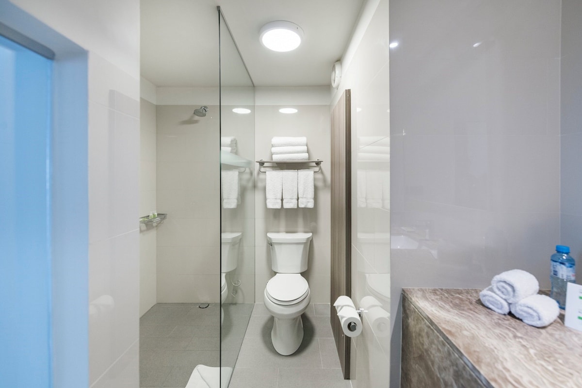 A modern bathroom with a glass shower enclosure, a toilet, and a marble countertop with towels.