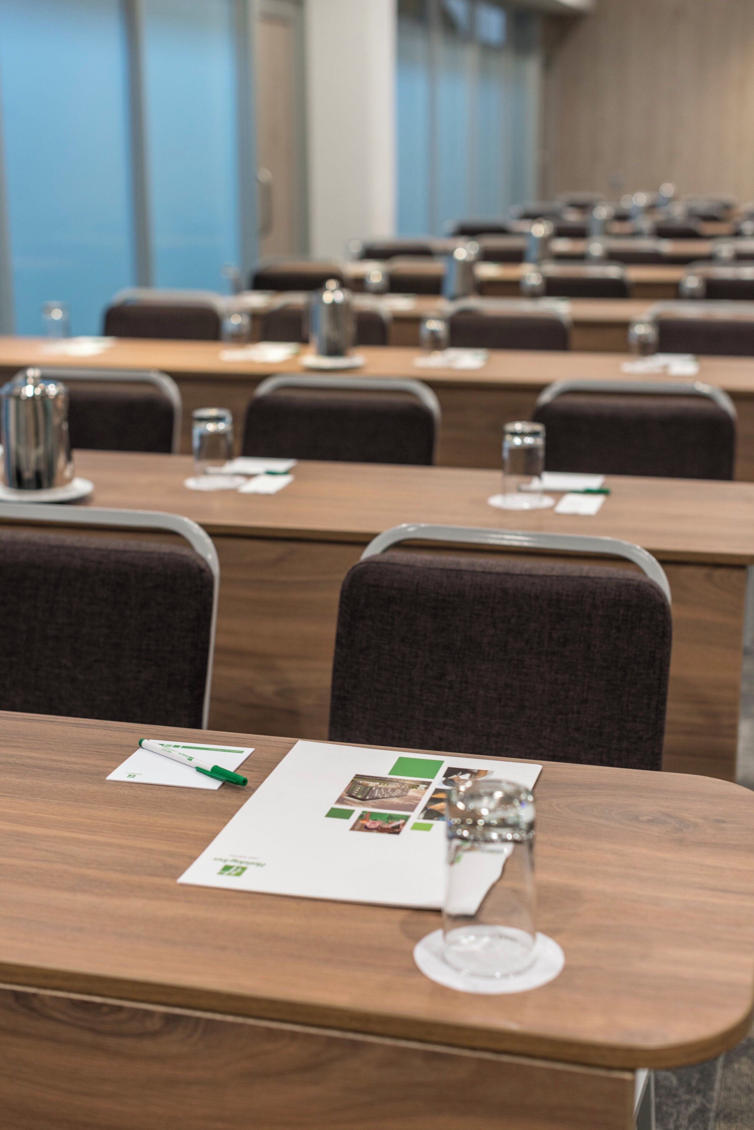 A conference room with rows of tables, each equipped with a glass, a pen, and a notepad.