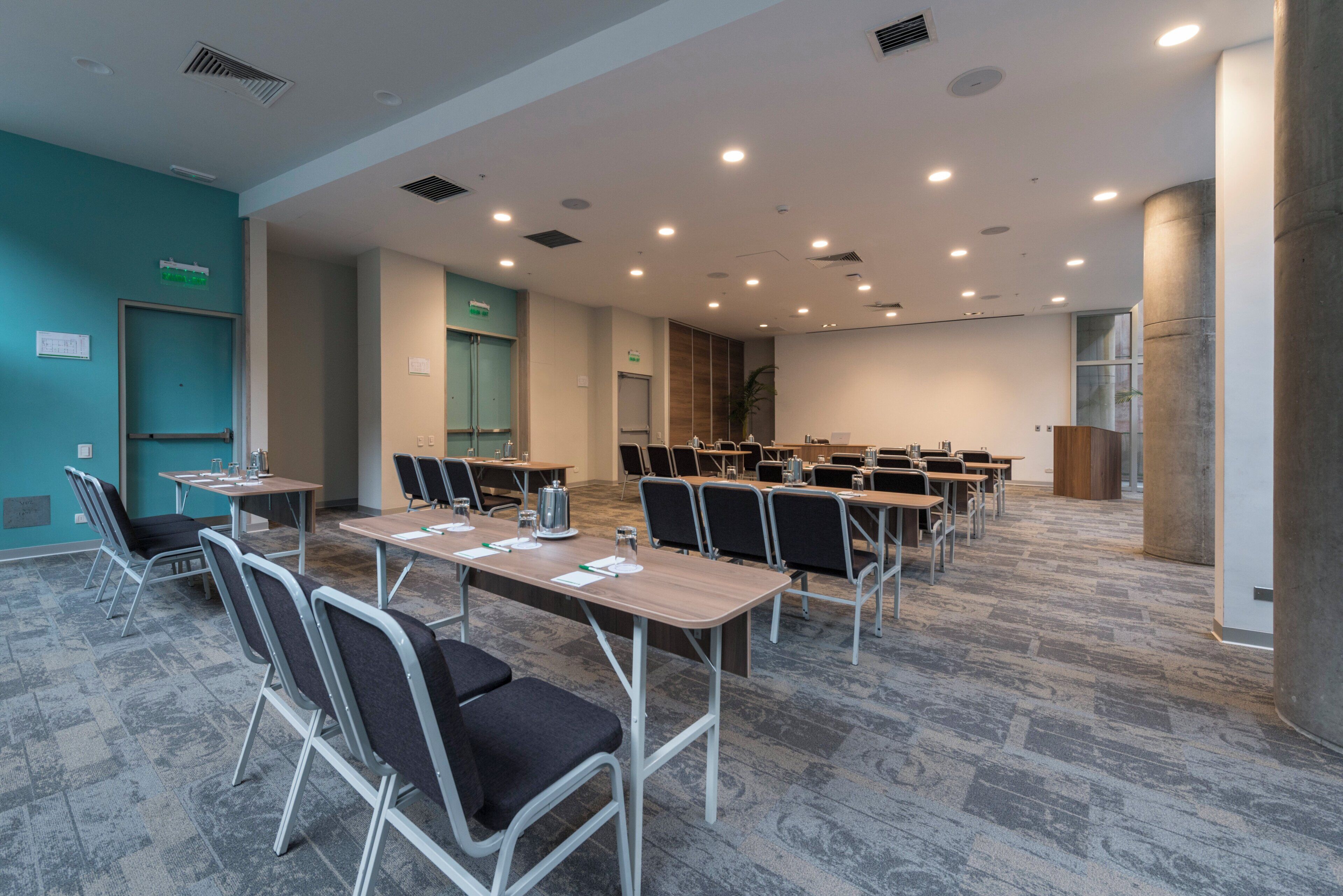 Un salón de conferencias con varias mesas y sillas, equipado con botellas de agua y blocs de notas.
