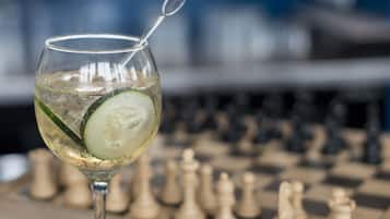 Un vaso de una bebida transparente con una rodaja de pepino y una pajita, sobre una superficie de mármol con un tablero de ajedrez al fondo.