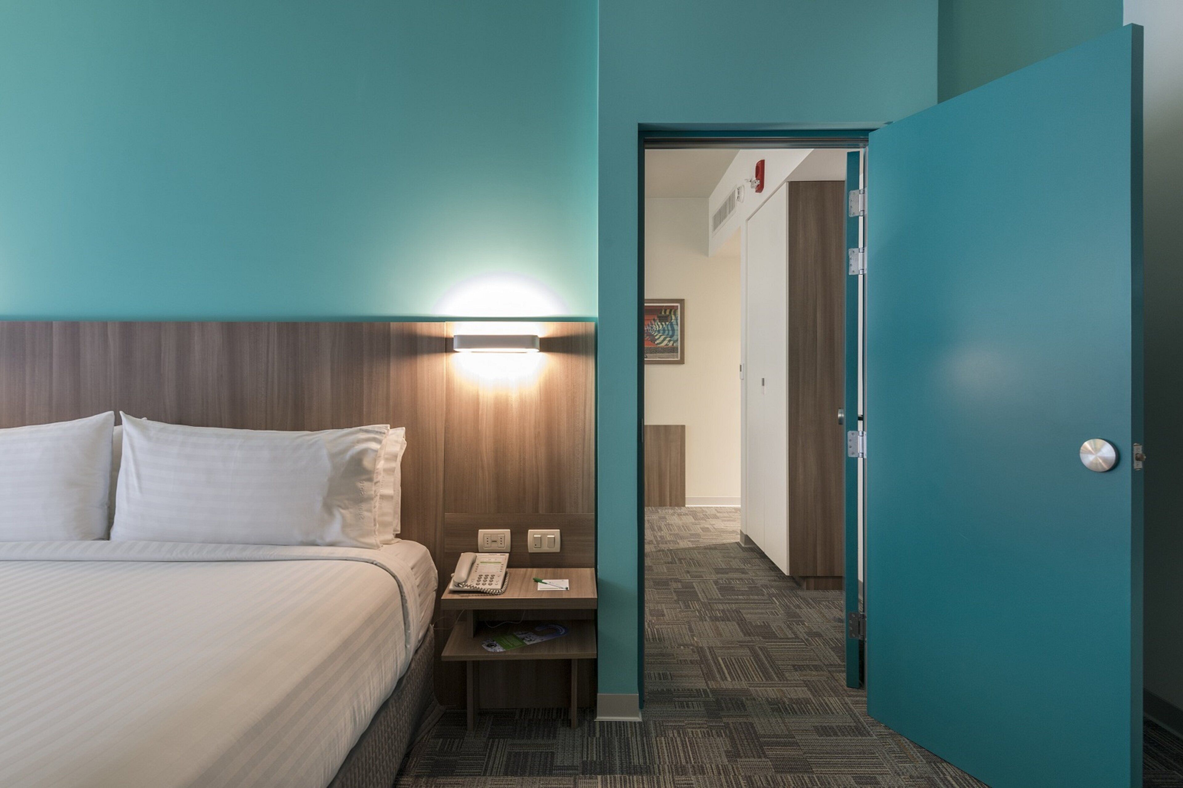 Ein Hotelzimmer mit Bett, Nachttisch und einer Tür zu einem anderen Raum.