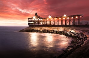 A waterfront building with a glass facade, a central tower, and a series of lights along the roofline.