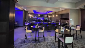 Zona de bar con diversas opciones de asientos, incluyendo mesas redondas y taburetes, además de un mostrador con una variedad de botellas.