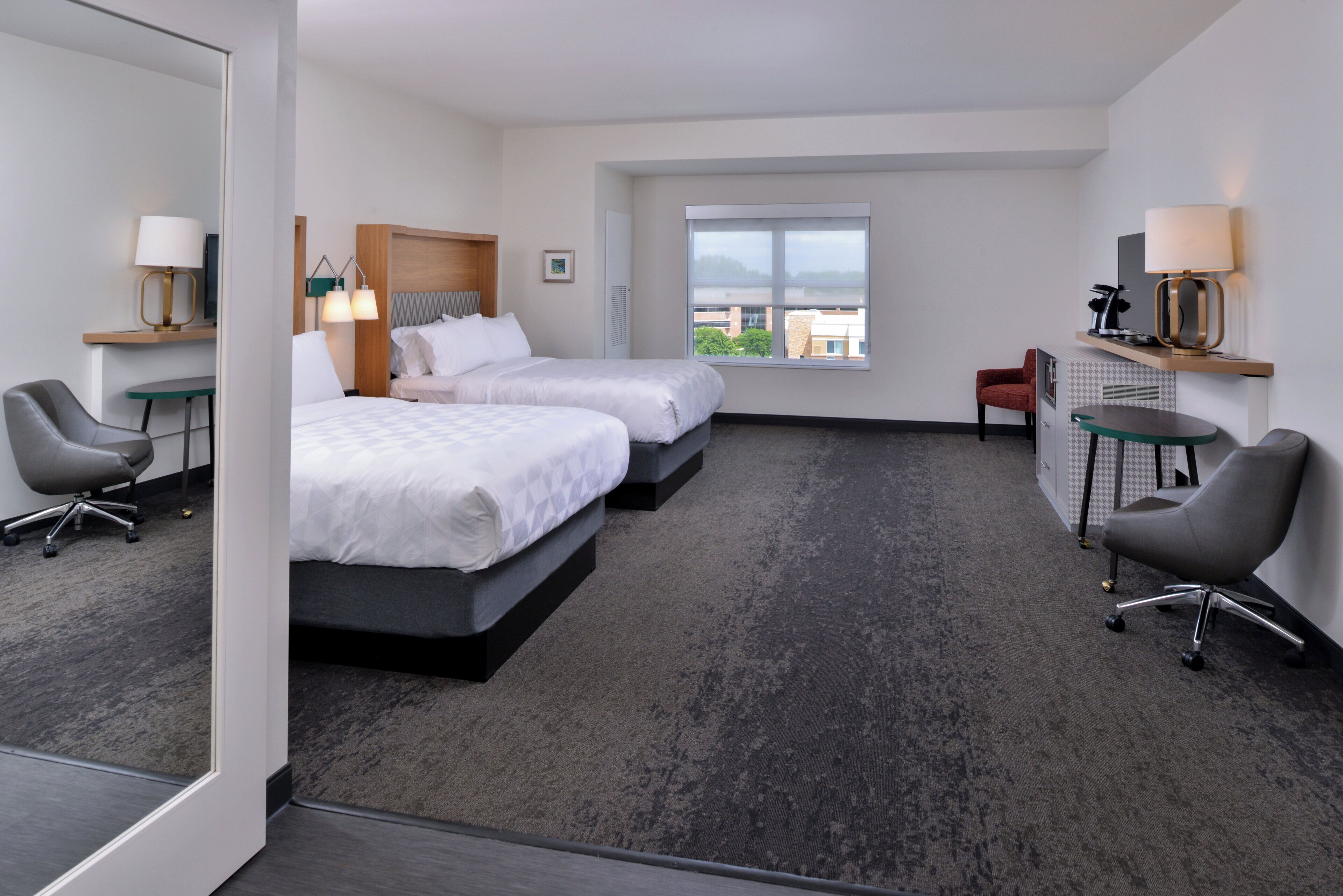 Une chambre d’hôtel avec deux lits, un bureau, une chaise, une fenêtre et une vue sur la ville.